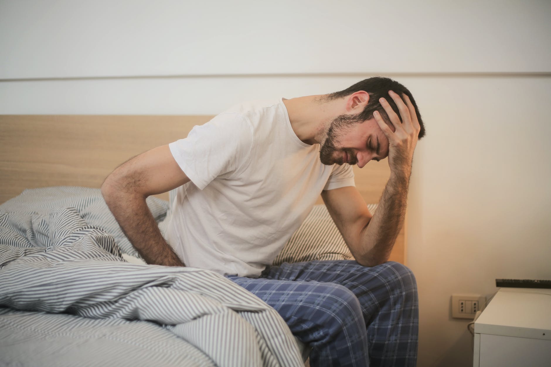 Tired man with a headache sitting on the edge of his bed.