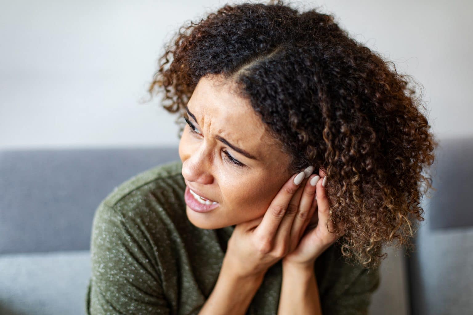 A woman experiencing ear pain, holding her hands up to her ear.