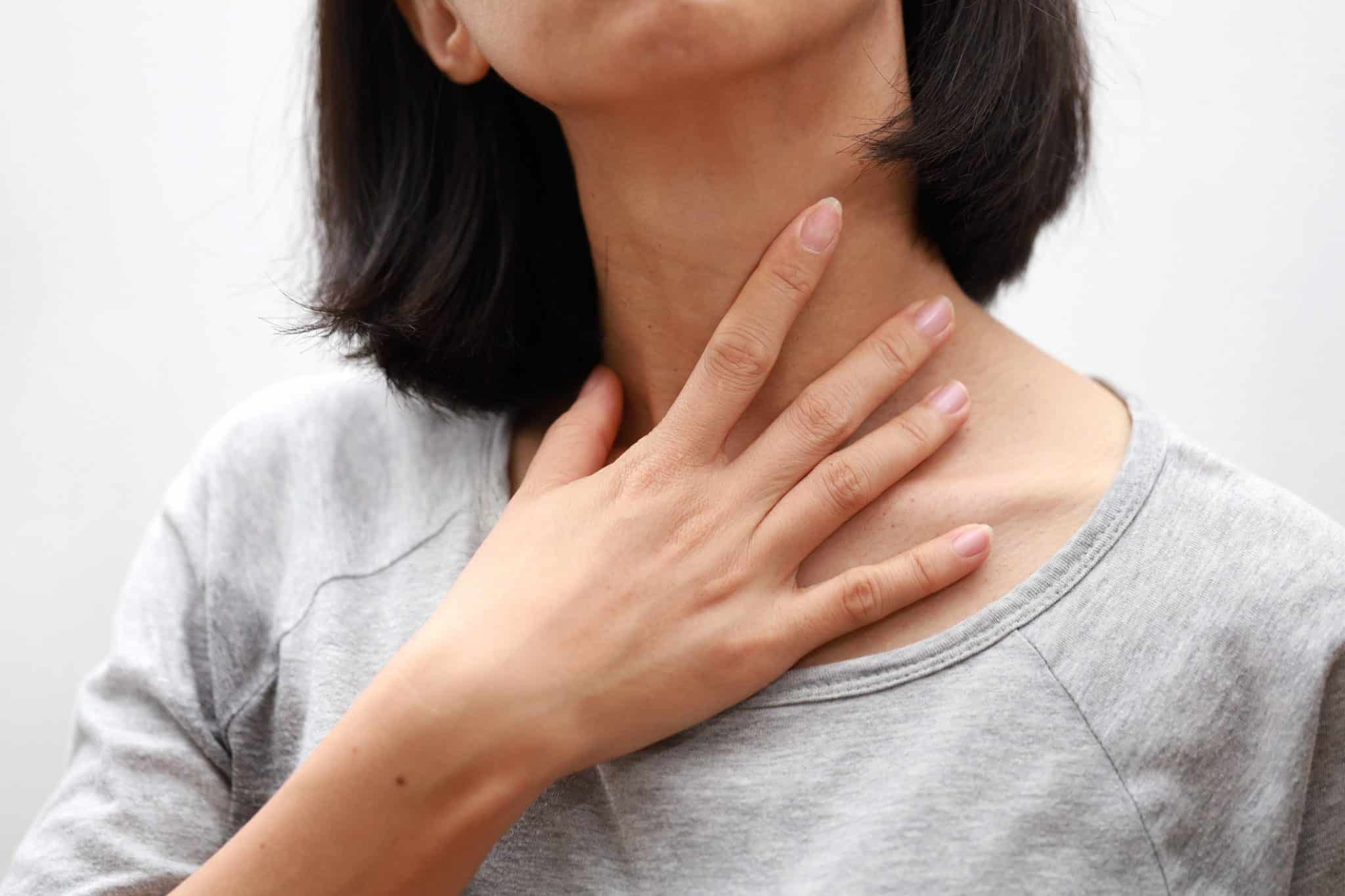 Closeup of a woman with laryngitis touching her hand to her throat.