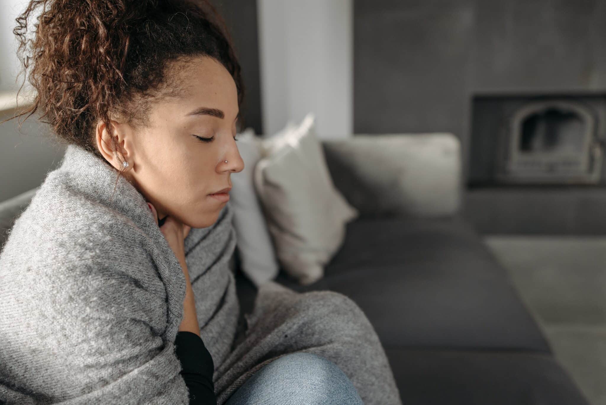 Woman wrapped up in a blanket while sick at home.