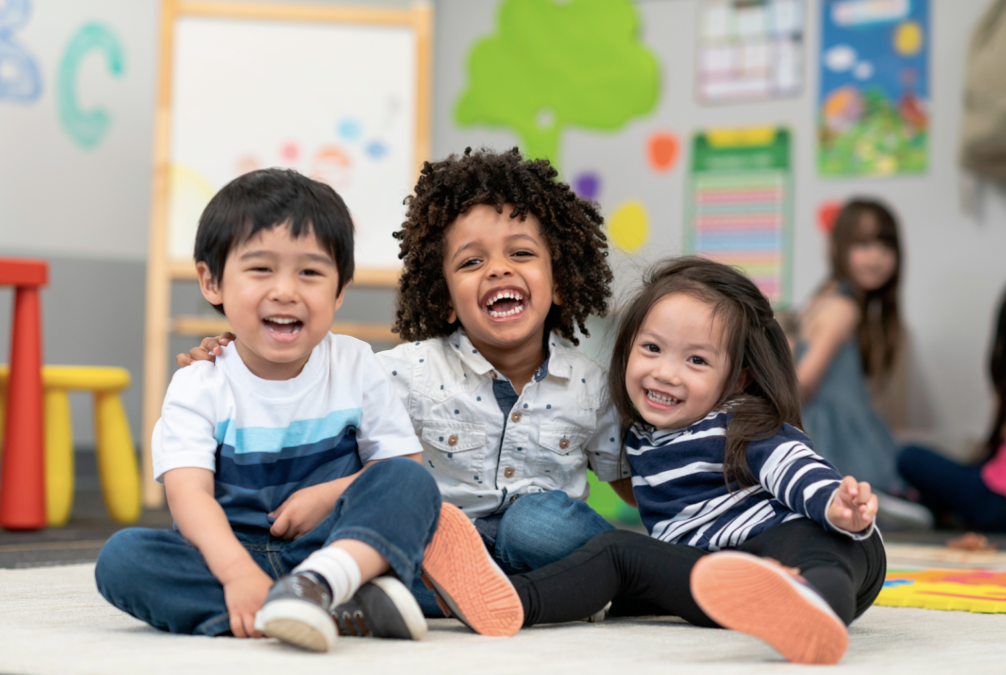three preschoolers sit together in their brightly colored classroom