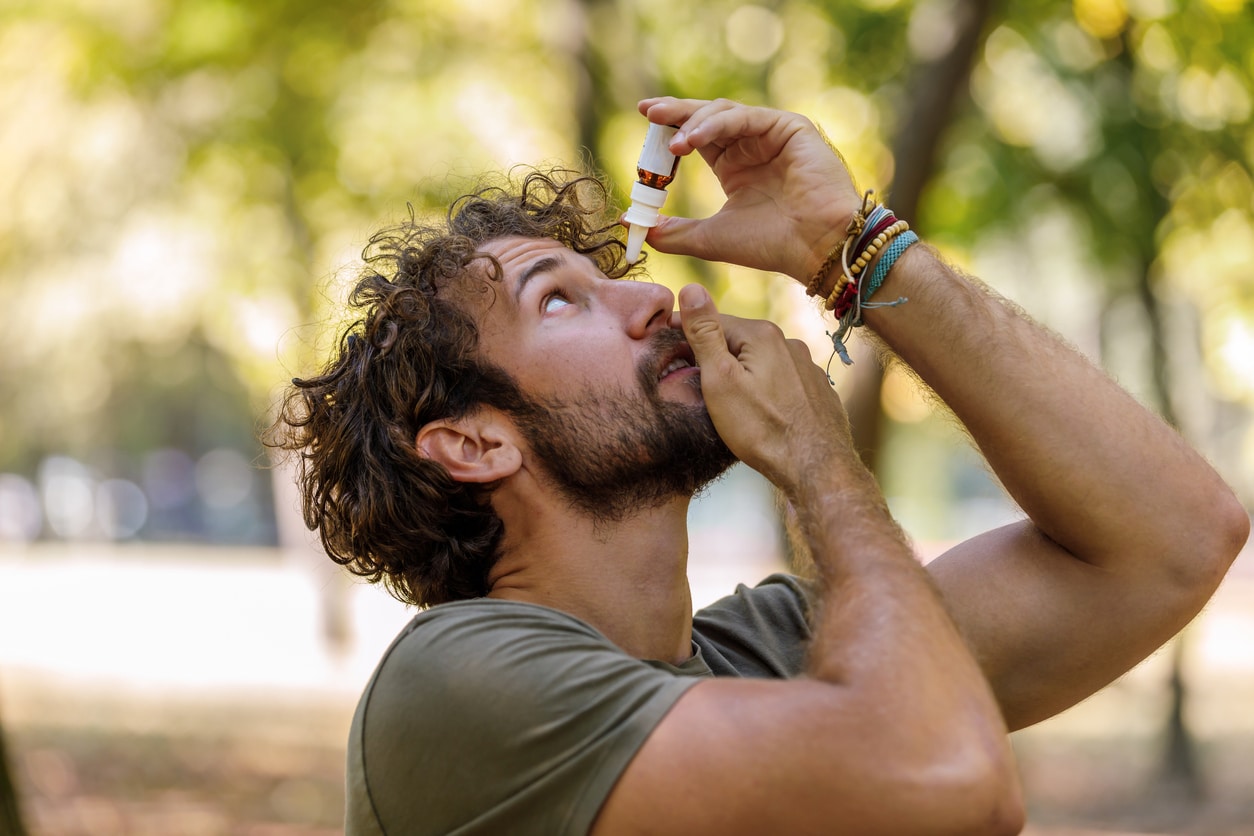 Man puts eye drops in eye in park