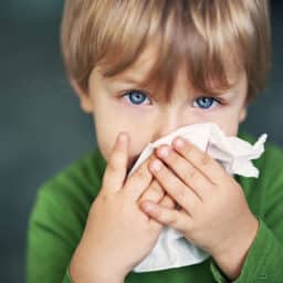 Young boy holds tissue to nose