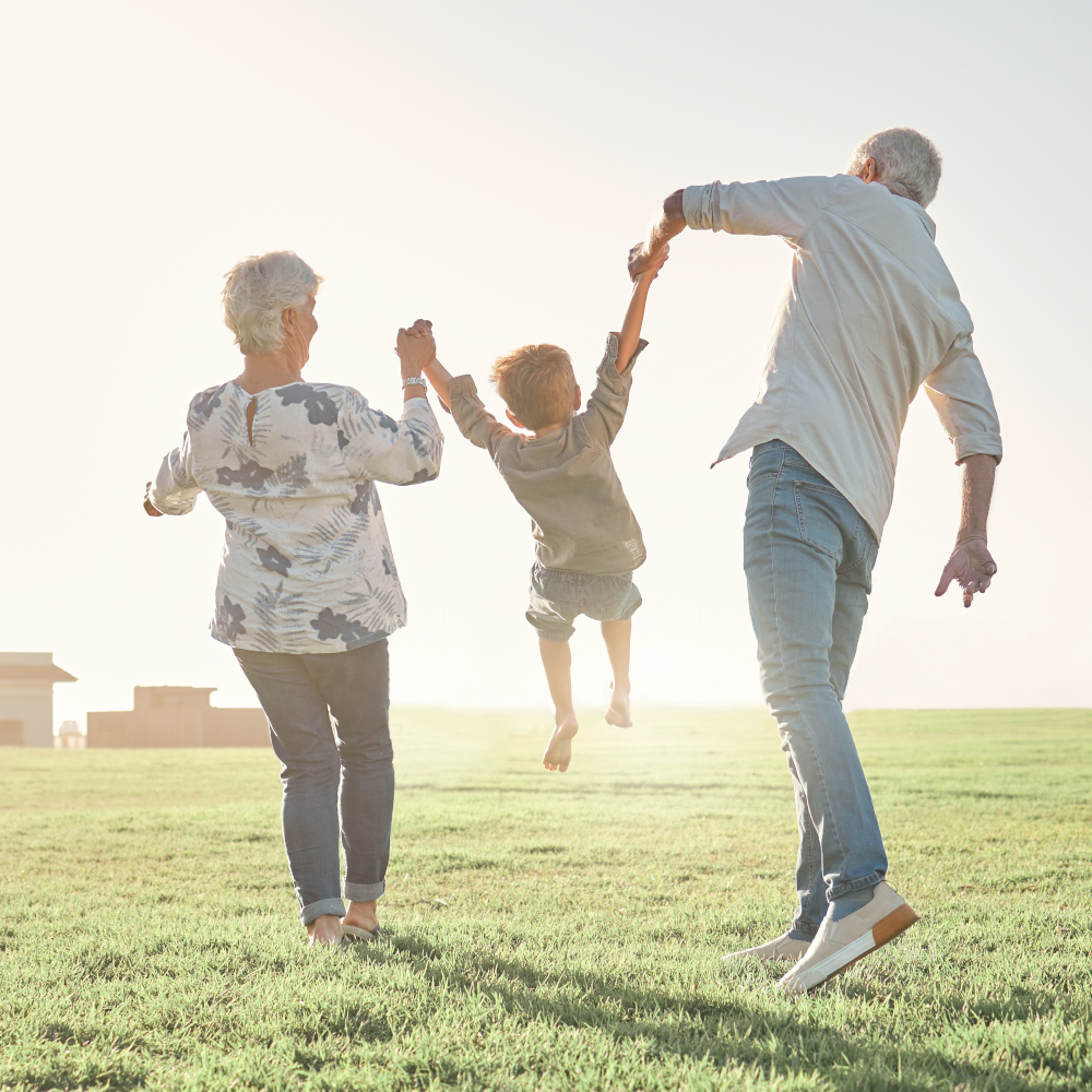 a child swings above the grass as they hold hands with their grandparents