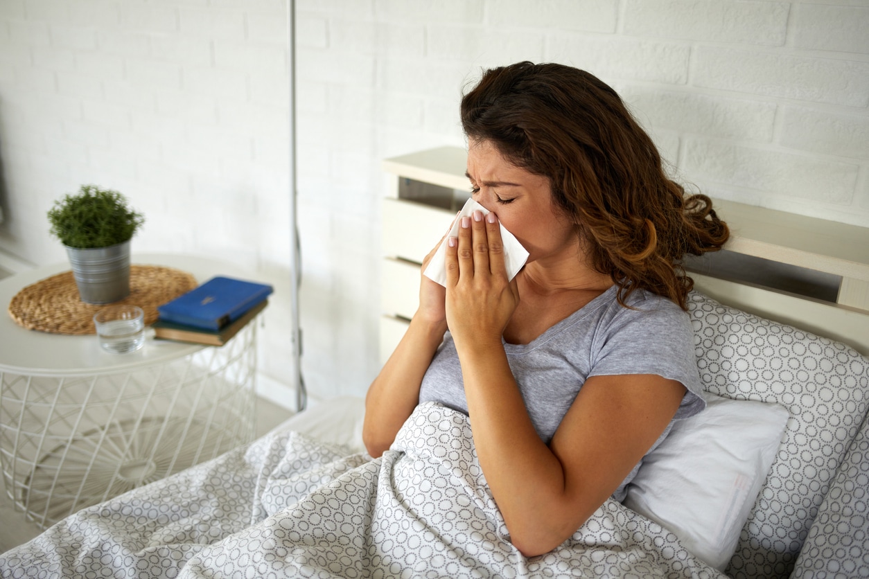 Woman lying in bed blowing her nose into a tissue