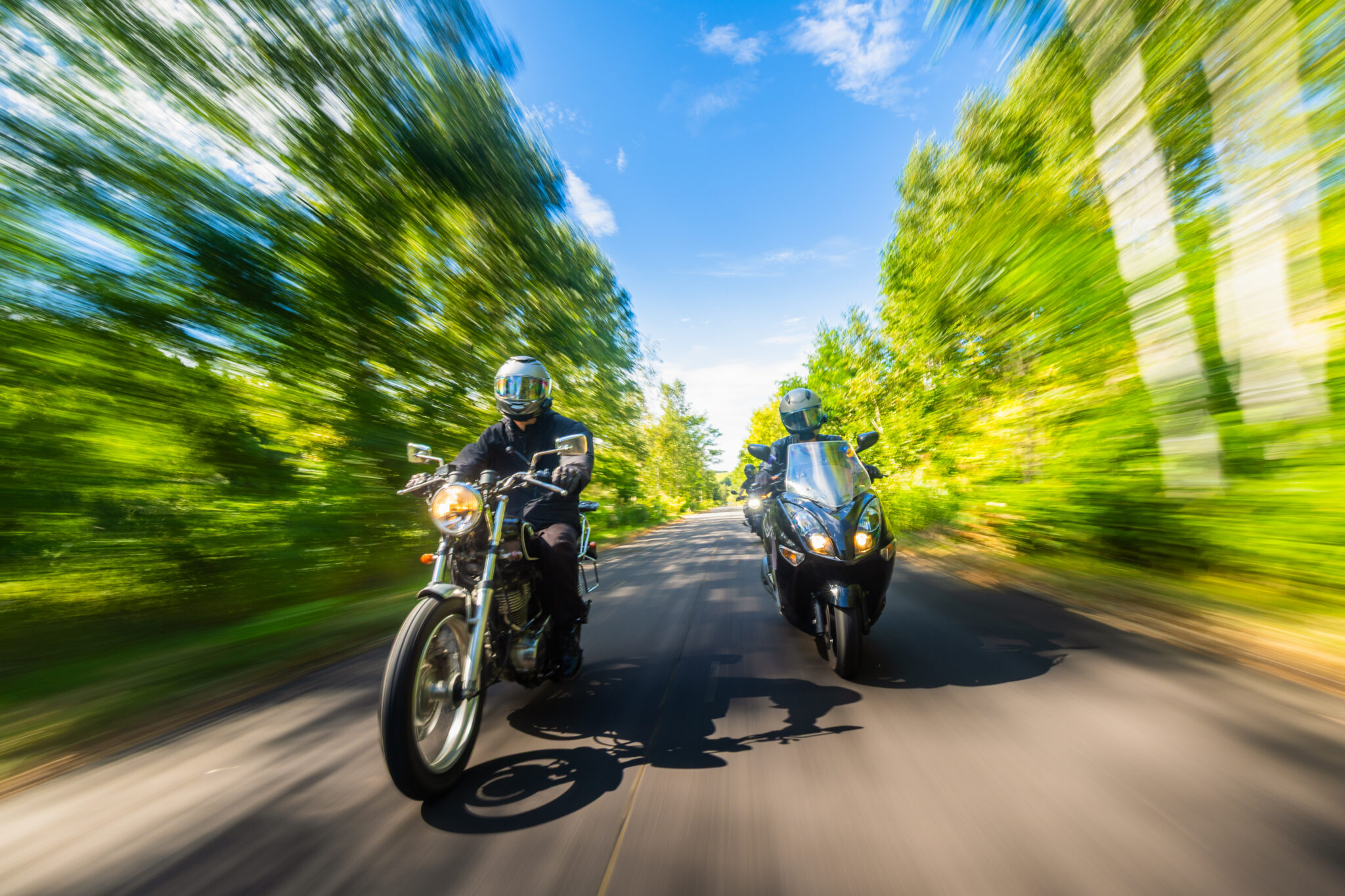 Two motorcyclists going for a fast ride down a tree-lined road.