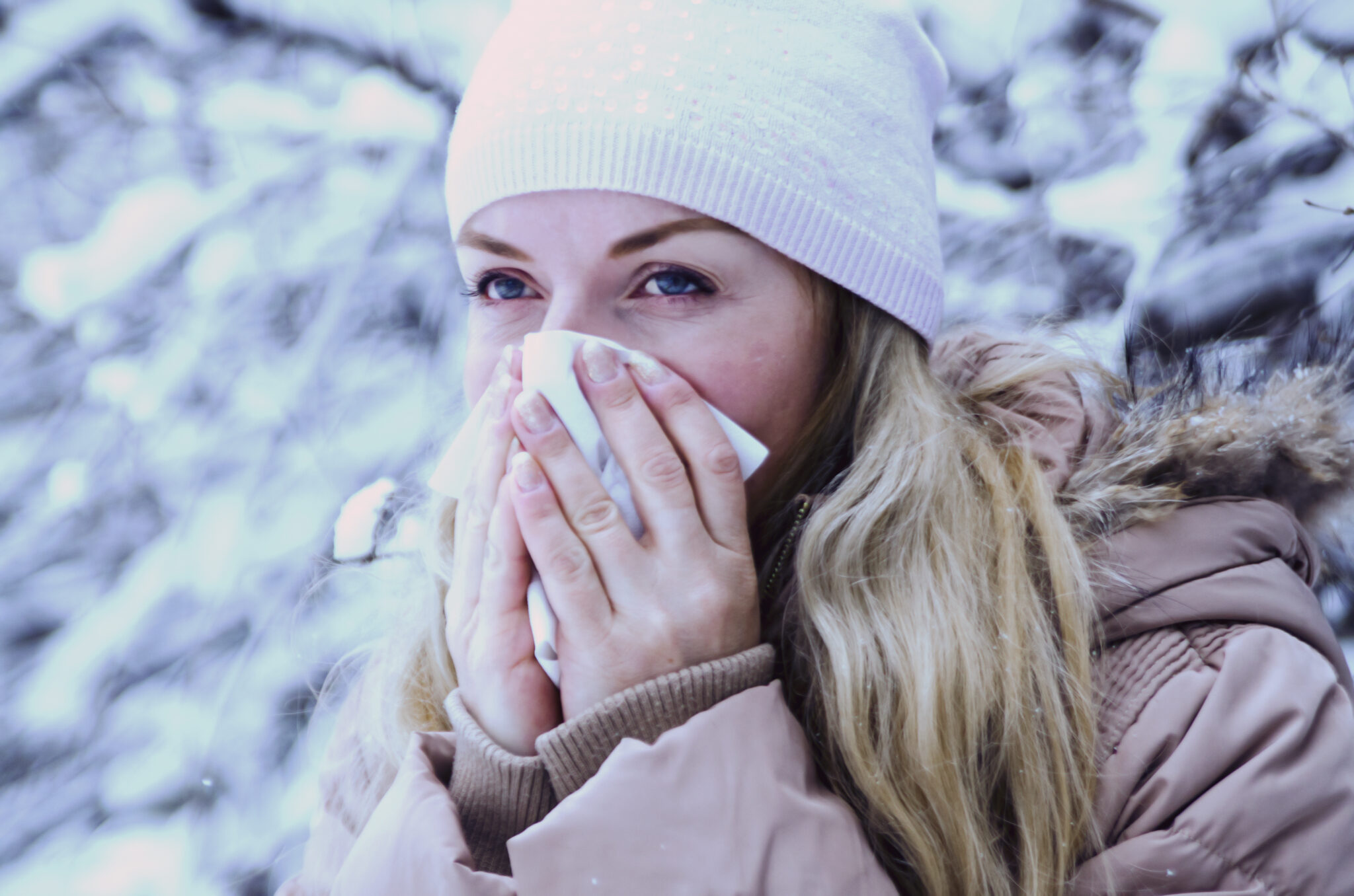 Woman experiencing a stuffy nose in the winter blows her nose into a tissue.